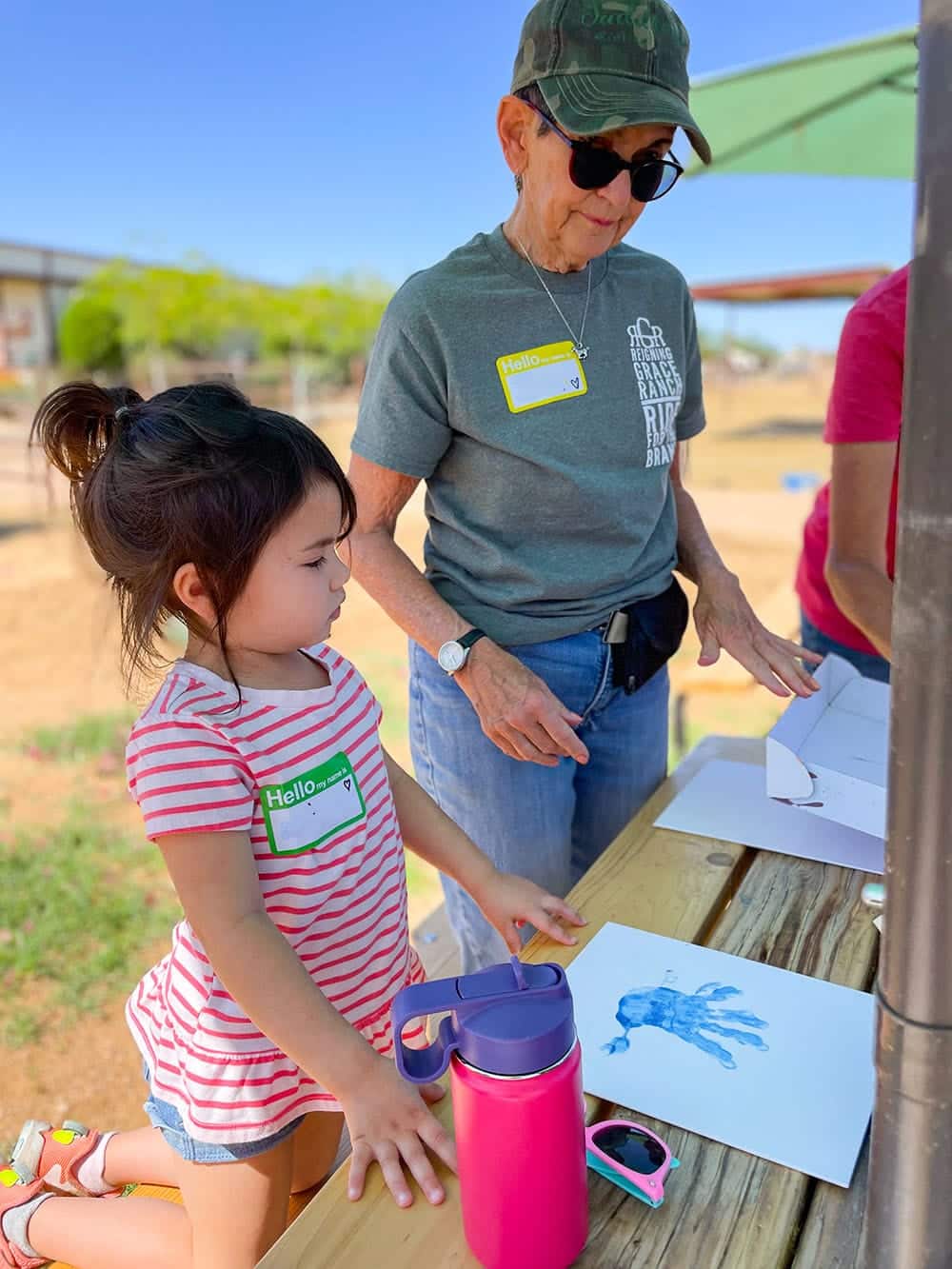 Woman helping a little girl with finger painting outdoors on a picnic table at the ranch