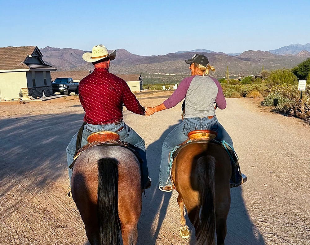 couple holding hands laughing while riding horses