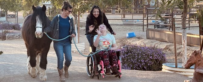 Sage pushing Maddison in her wheelchair on the ranch walking a horse