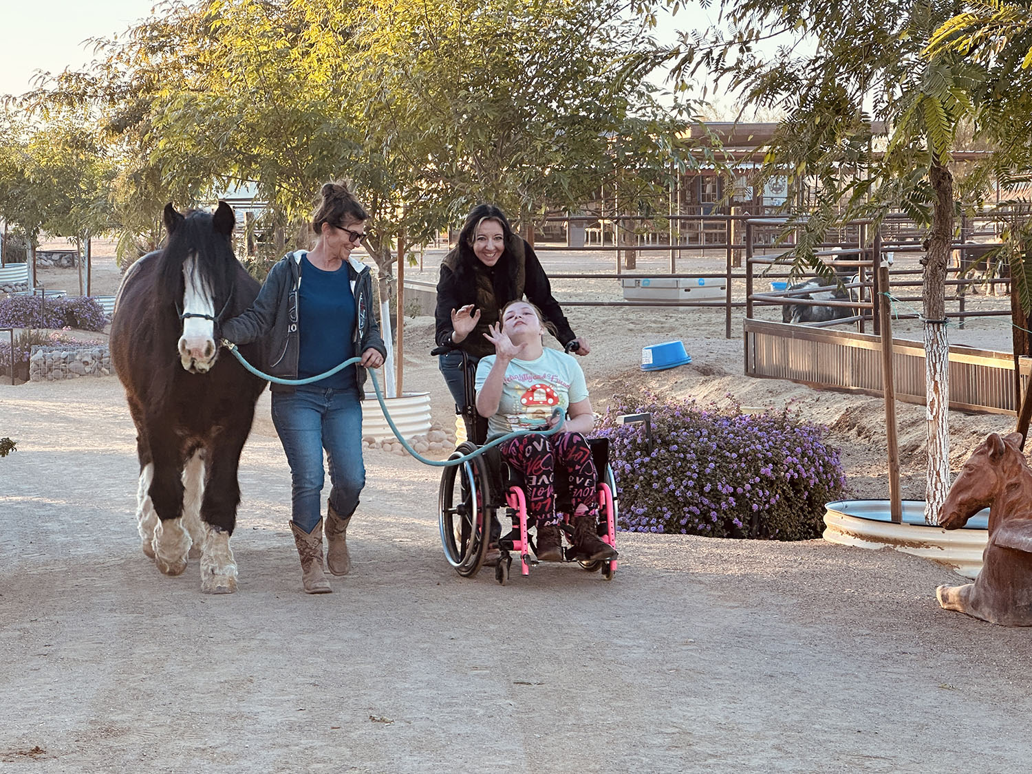 Sage pushing Maddison in her wheelchair on the ranch walking a horse